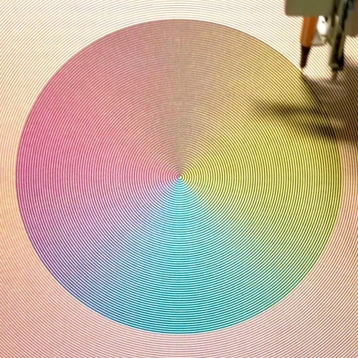 A printing in progress view, showing three overlapping spirals (yellow, magenta, cyan) being overlaid with a fourth black layer.